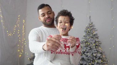 Yeni yılda oğluyla birlikte Afrika kökenli Amerikalı bir adam Noel 'i ağaç kenarında kutluyor, baba ve çocuk birlikte seviniyor ve yeni yıl gelenekleriyle eğleniyor.