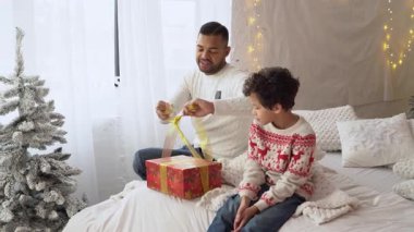 Afrika kökenli Amerikalı baba ve oğul yeni yıla hazırlanıyor ve evde bir hediye kutusuna fiyonk bağlıyorlar.