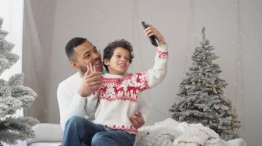 Afrika kökenli Amerikalı baba ve oğul video konuşarak Noel ağacının yakınında mutlu yıllar diliyor. Noel 'i evde kutluyor ve akıllı telefondan selfie çekiyor.
