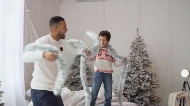 Afro-Amerikan erkek ve oğlu yeni yılı evde kutluyor ve süslerle dans ediyor, çocuk ve baba eğleniyor ve Noel 'de oynuyorlar.