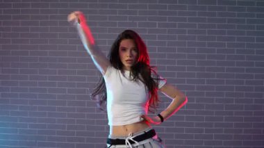 Genç çılgın kız duvarın arkasında dans ediyor. Neon ışıklandırmada arka planda. Kadın koreograf müzik yapıyor ve dans stüdyosunda caz funk 'ı çalıyor.