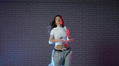 Genç çılgın kız duvarın arkasında dans ediyor. Neon ışıklandırmada arka planda. Kadın koreograf müzik yapıyor ve dans stüdyosunda caz funk 'ı çalıyor.