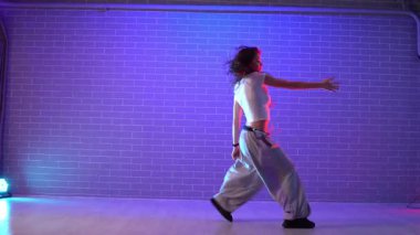 Genç çılgın kız duvarın arkasında dans ediyor. Neon ışıklandırmada arka planda. Kadın koreograf müzik yapıyor ve dans stüdyosunda caz funk 'ı çalıyor.