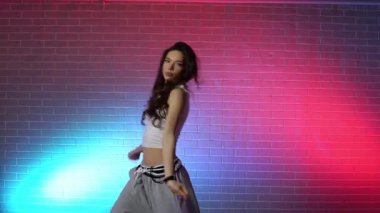 Genç kız koreograf dans ediyor, neon ışıkta hip hop yapıyor, kadın kamera önünde şarkı söylüyor ve karanlık stüdyoda caz funk dansı yapıyor.