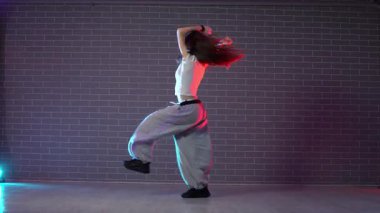 Genç çılgın kız duvarın arkasında dans ediyor. Neon ışıklandırmada arka planda. Kadın koreograf müzik yapıyor ve dans stüdyosunda caz funk 'ı çalıyor.