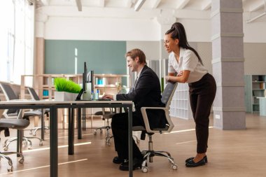 Masada oturan ve bilgisayarla çalışan iki ofis çalışanı. Afrikalı Amerikalı bayan patron, genç çalışanın internet üzerinden bilgi bulmasına ve öğretmenlik yapmasına yardım ediyor.