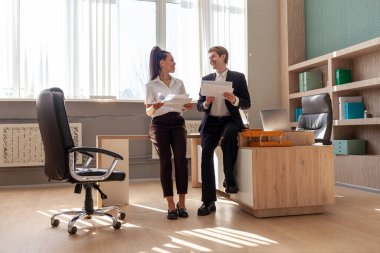 Ofis çalışanları iş kıyafetleri içinde toplantıda belgeleri tartışıyorlar, Afrikalı Amerikalı kadın ve beyaz adam rapor hakkında konuşup duruyorlar, genel görüş...