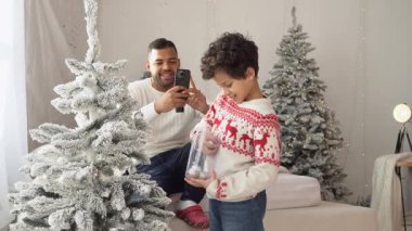 Afrikalı Amerikalı bir adam, oğlunun Noel ağacını süslediğini ve merhaba dediğini filme alır. Babası Noel 'de çocuğun akıllı telefon fotoğrafını çeker.