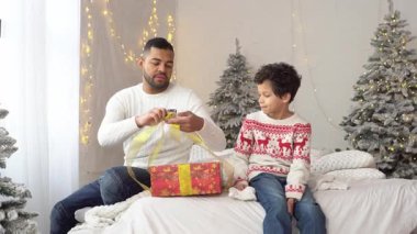 Afrika kökenli Amerikalı baba ve oğul yeni yıla hazırlanıyor ve evde bir hediye kutusuna fiyonk bağlıyorlar.