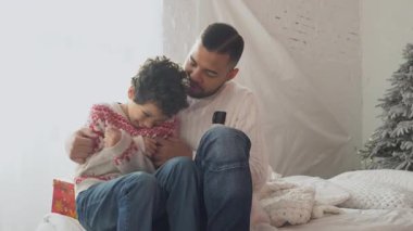 Noel kıyafetleri içinde Afrikalı Amerikalı baba ve oğul evde oturuyor ve yılbaşından önce konuşuyor, Noel 'de çocukla eğleniyor ve gülümsüyor.