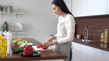 Önlüklü genç Asyalı kadın evde salata için biber kesiyor, Koreli kız evde sağlıklı yemekler pişiriyor ve sebze kesiyor.