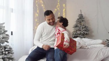 Afrikalı Amerikalı çocuk yeni yıl süveteri veriyor ve babaya evde mutlu noeller diliyor, yeni yılı kutluyor ve sürpriz bir şekilde seviniyor.