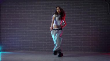 Genç kız koreograf dans ediyor, neon ışıkta hip hop yapıyor, kadın kamera önünde şarkı söylüyor ve karanlık stüdyoda caz funk dansı yapıyor.