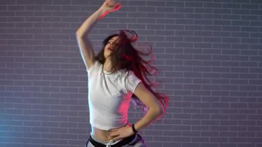 Genç kız koreograf dans ediyor, neon ışıkta hip hop yapıyor, kadın kamera önünde şarkı söylüyor ve karanlık stüdyoda caz funk dansı yapıyor.