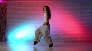 Genç kız koreograf dans ediyor, neon ışıkta hip hop yapıyor, kadın kamera önünde şarkı söylüyor ve karanlık stüdyoda caz funk dansı yapıyor.