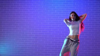 Genç çılgın kız duvarın arkasında dans ediyor. Neon ışıklandırmada arka planda. Kadın koreograf müzik yapıyor ve dans stüdyosunda caz funk 'ı çalıyor.