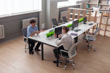 İş kıyafetleri içinde iki genç iş adamı masada oturup konuşur, ofis çalışanları ve iş arkadaşları iletişim kurar ve iş hakkında tartışırlar.