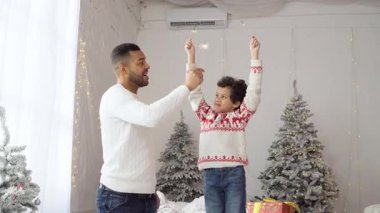 Yeni yılda oğluyla birlikte Afrika kökenli Amerikalı bir adam Noel 'i ağaç kenarında kutluyor, baba ve çocuk birlikte seviniyor ve yeni yıl gelenekleriyle eğleniyor.