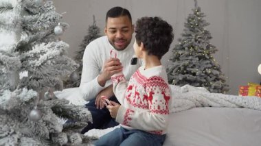 Yılbaşı arifesinde Noel ağacının yanında şeker yiyen Afrikalı baba ve oğul Noel 'i evde birlikte kutluyor ve tatlı yiyorlar.