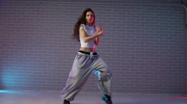 Genç çılgın kız duvarın arkasında dans ediyor. Neon ışıklandırmada arka planda. Kadın koreograf müzik yapıyor ve dans stüdyosunda caz funk 'ı çalıyor.