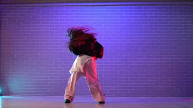 Genç kız koreograf dans ediyor, neon ışıkta hip hop yapıyor, kadın kamera önünde şarkı söylüyor ve karanlık stüdyoda dans çalışıyor.