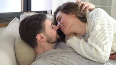 Genç bir çift kanepede sarılıyor ve konuşuyor, mutlu bir adam ve kadın ilişki içinde, konuşuyor ve öpüşüyor, yakın plan.