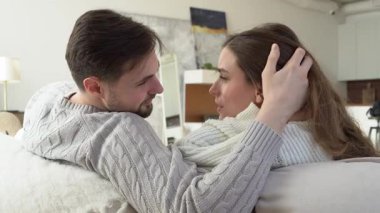 Genç bir çift kanepede sarılıyor ve konuşuyor, mutlu bir adam ve kadın ilişki içinde, konuşuyor ve öpüşüyor, yakın plan.