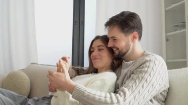 Genç bir çift kanepede sarılıyor ve konuşuyor, mutlu bir adam ve kadın ilişki içinde, konuşuyor ve öpüşüyor, yakın plan.