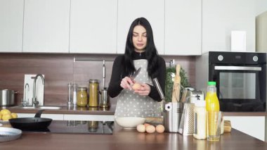 Önlüklü genç bir kadın mutfakta tavuk yumurtalarını tabağa koyar, kız omlet hazırlar ve evde yumurtalarını kabuklarından ayırır.