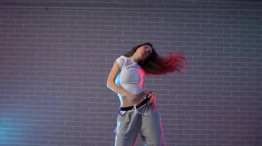 Genç kız koreograf dans ediyor, neon ışıkta hip hop yapıyor, kadın kamera önünde şarkı söylüyor ve karanlık stüdyoda caz funk dansı yapıyor.