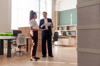 Ofis çalışanları iş kıyafetleri içinde yürüyorlar raporları tartışıyorlar ve ellerinde belgeler tutuyorlar, Afrikalı Amerikalı kadın ve genç Avrupalı erkek toplantıda konuşuyorlar ve planlıyorlar, genel plan