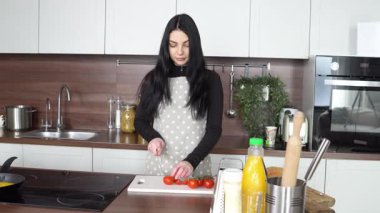 Önlüklü genç bir kadın mutfakta vişneli domates keser, kız evde domatesli omlet hazırlar.