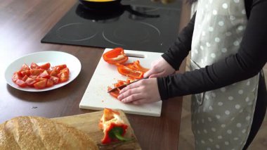 Önlüklü genç bir kadın mutfakta kırmızı dolmalık biber, evde yemek pişiriyor ve sebze doğruyor.