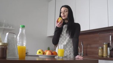 Önlüklü genç kadın mutfakta elma yer, kız meyveyi yer ve evde dinlenir.