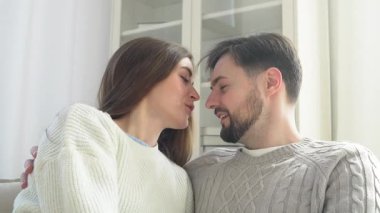 Genç bir çift kanepede sarılıyor ve konuşuyor, mutlu bir adam ve kadın ilişki içinde, konuşuyor ve öpüşüyor, yakın plan.