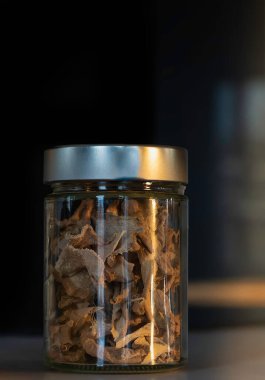 Metalik kapaklı cam bir kavanozda kurutulmuş zencefil dilimleri. Yiyecek ve içecekler için egzotik çeşni. Koyu yiyecek fotoğrafçılığı