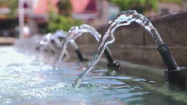 Çeşmeden akan su. Su sıçrar ve arka plan bulanıklaşır. 4K çözünürlüğü. Seçici odak