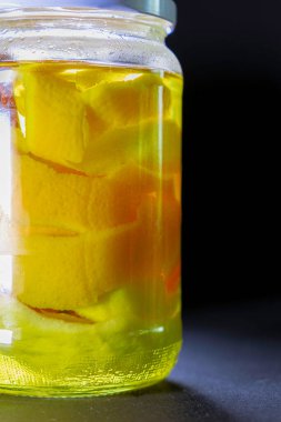 Siyah arka planda turunçgil kabuklu cam kavanoz ve votka. Likör ayrıntıları. Konserve konsepti. Kapat.