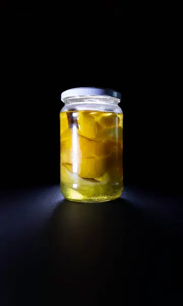 Glass jar with citrus peel and vodka on a black background. Liquor elaboration. Canning concept