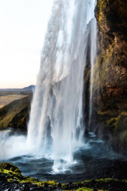 Bir şelale kayalık bir uçurumdan aşağı akıyor. Su beyaz ve berrak, ve sis yerden yükseliyor. Sahne huzurlu ve huzurlu. Altın Çember, İzlanda.