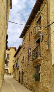 Solunda bir bina ve sağında başka bir bina olan dar bir ara sokak. Binalar taştan yapılmış ve balkonları var.