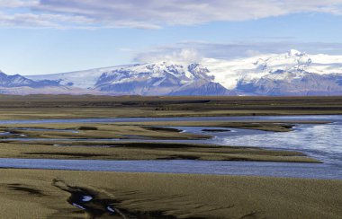 Arka planda mavi gökyüzü olan güzel bir dağ sırası. İçinden nehir akan bir çöl manzarası. Dağlar karla kaplı ve gökyüzü berrak.