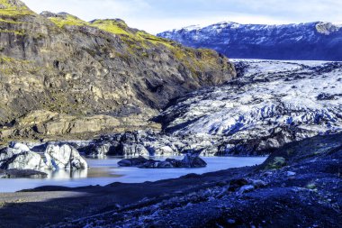 Büyük bir su kütlesi ve İzlanda 'daki Solheimajokull buzulu ile güzel bir manzara. Su mavi ve dağ yosunlarla kaplı.