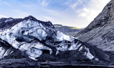 Üzerinde büyük bir buz duvarı olan bir dağ. Solheimajokull Buzulu, İzlanda. Gökyüzü mavi ve güneş parlıyor.