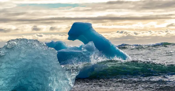 Okyanusta büyük bir buz parçası yüzüyor. Buz daha küçük buz parçalarıyla çevrili, güzel ve huzurlu bir manzara yaratıyor. Su sakin ve gökyüzü bulutlu.