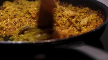 İçinde pirinç ve et olan bir tencere yemek. Pirinci tahta kaşıkla kaşıklamak. Geleneksel İspanyol mutfağı. Paella. 4K video