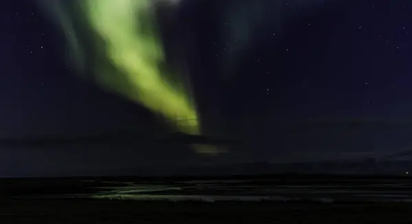 stock image A beautiful aurora borealis is visible in the sky above a large body of water. Iceland by night.