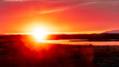 Gökyüzünde büyük bir güneşle gölün üzerinde güzel bir gün batımı. Gökyüzü turuncu ve pembe renklerin karışımıdır. Huzurlu ve huzurlu bir atmosfer yaratır.