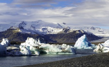 Önünde büyük bir su kütlesi olan güzel bir dağ manzarası. Su buz ve karla kaplı. Huzurlu ve huzurlu bir atmosfer yaratıyor.