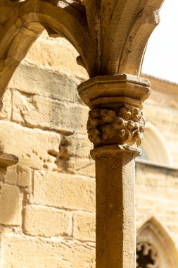 Üzerinde çiçek deseni olan taş bir sütun. Sütun bir binanın önünde yer almaktadır. Ortaçağ mimarisi. Kilise Sanatının Ayrıntıları